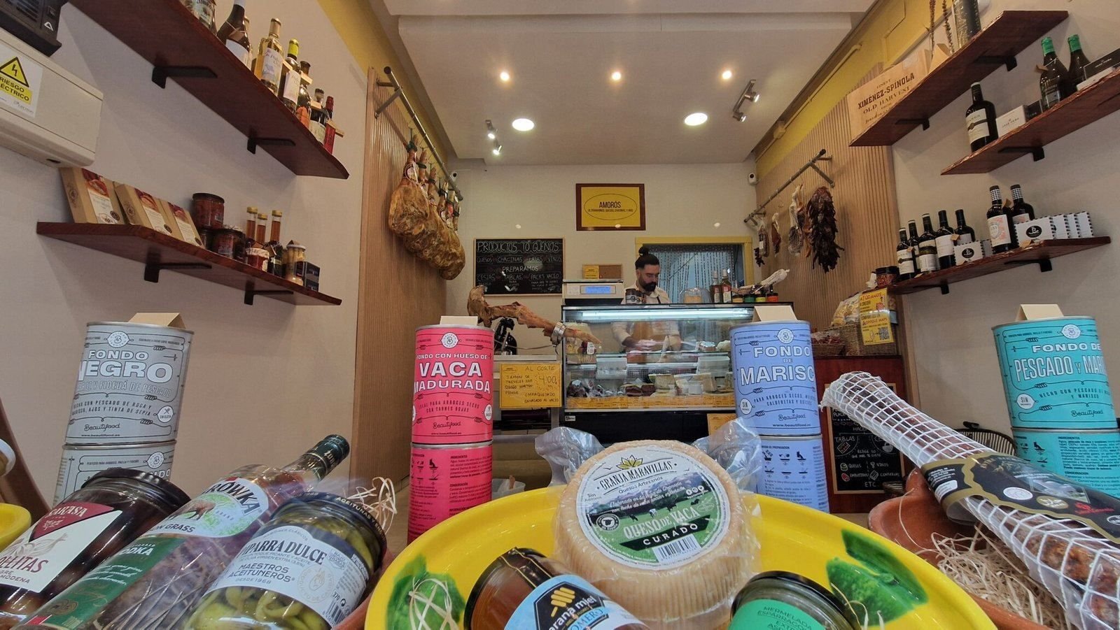 Interior de la tienda: estanterías con vinos y conservas, jamones colgados y el mostrador de quesos